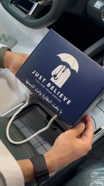 Navy Just Believe gift box with umbrella logo, held inside a car