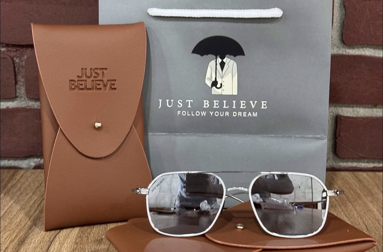 Cognac leather pouch embossed Just Believe, next to the branded shopping bag with the umbrella logo